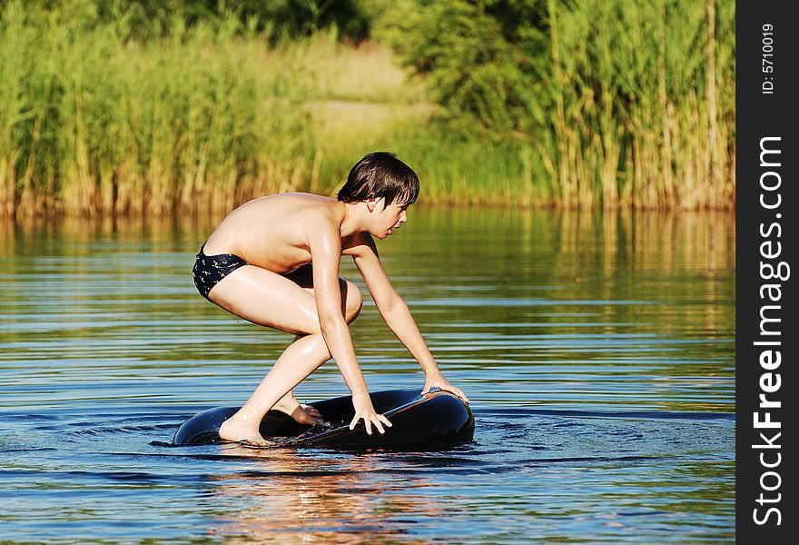 The boy trying to stand up on a tube that floats in a middle of a small lake. The boy trying to stand up on a tube that floats in a middle of a small lake.