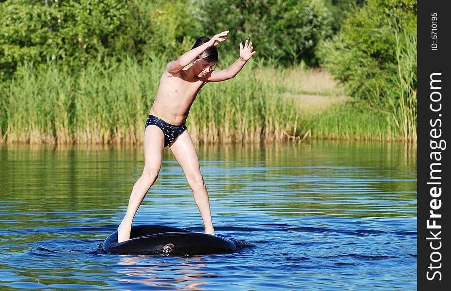 The boy trying to keep the balance standing on a tube that floats in a middle of a small lake. The boy trying to keep the balance standing on a tube that floats in a middle of a small lake.