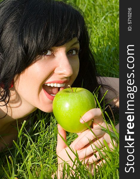 Pretty woman eating green apple on the summer glade