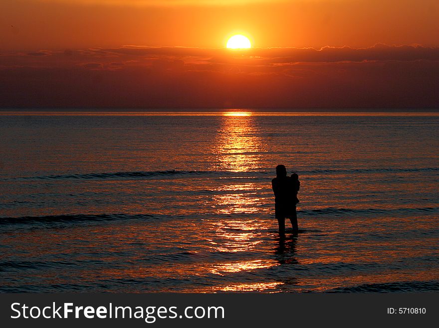A mother and small child wade into the water during a beautiful sunset. A mother and small child wade into the water during a beautiful sunset