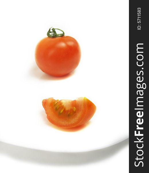 A slice of tomato and a blurred whole one on a white plate and isolated on white background. A slice of tomato and a blurred whole one on a white plate and isolated on white background