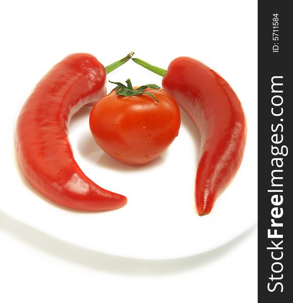 Two fresh chili peppers and a ripe tomato on a white plate and isolated on white background. Two fresh chili peppers and a ripe tomato on a white plate and isolated on white background