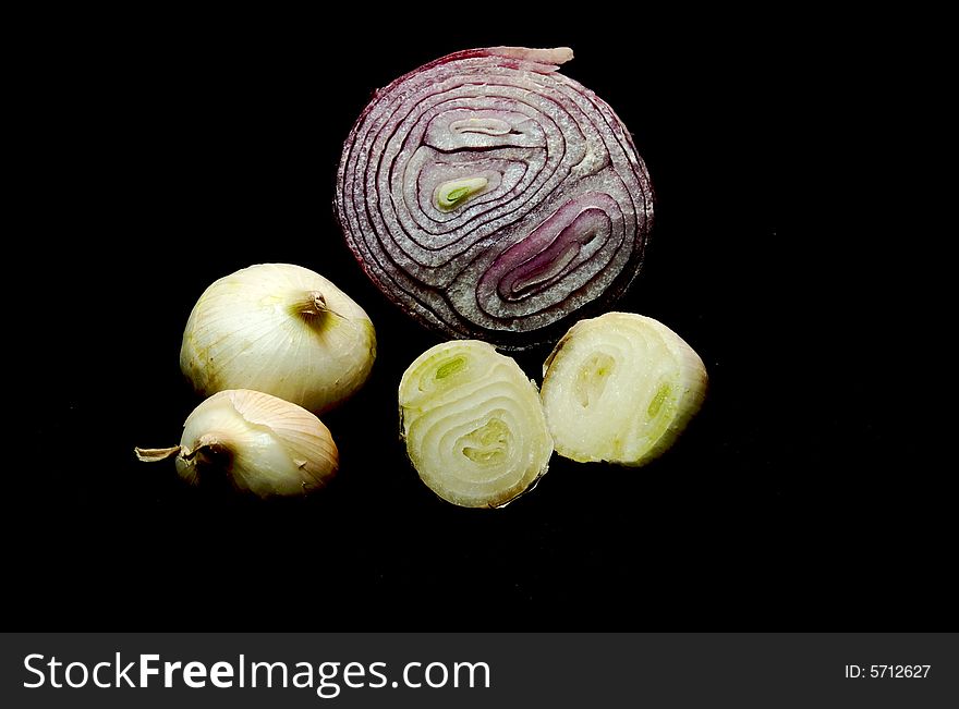 A sliced red onion surrounded by smaller yellow onions, on a black (000000) background.