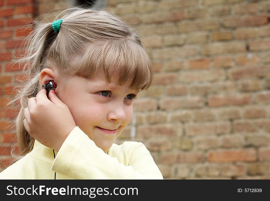 The girl listens to music on a background of a brick wall