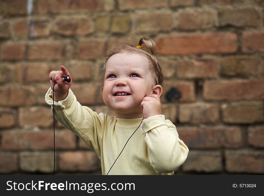 The baby listens to music on a background of a brick wall. The baby listens to music on a background of a brick wall