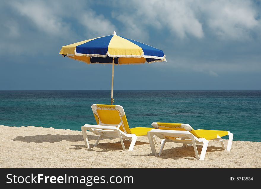 A photo of two chairs and beach umbrella on the sand