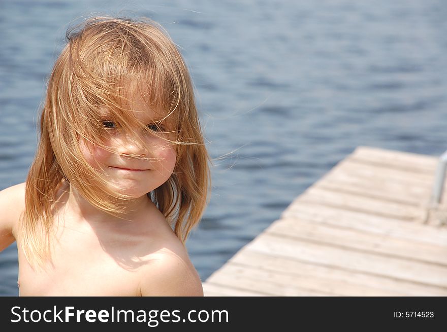 Smiling 3 year old girl with her hair messed on the river pier. Smiling 3 year old girl with her hair messed on the river pier