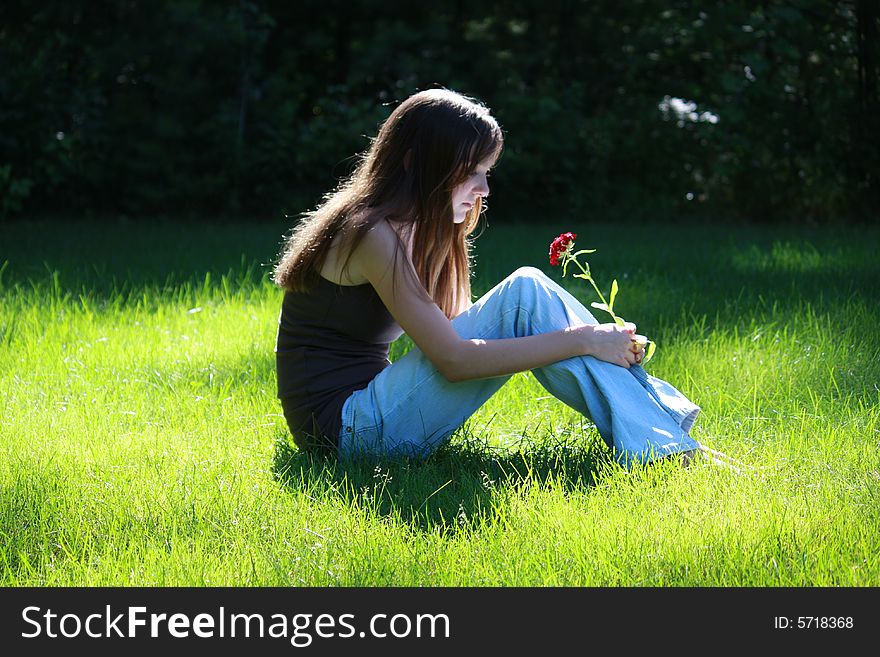Female teenager sitting in the grass looking thoughtfully at a flower. Female teenager sitting in the grass looking thoughtfully at a flower.