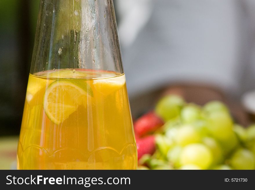 Cold jar of ice tea sits on a table with fruit in the background. Cold jar of ice tea sits on a table with fruit in the background.