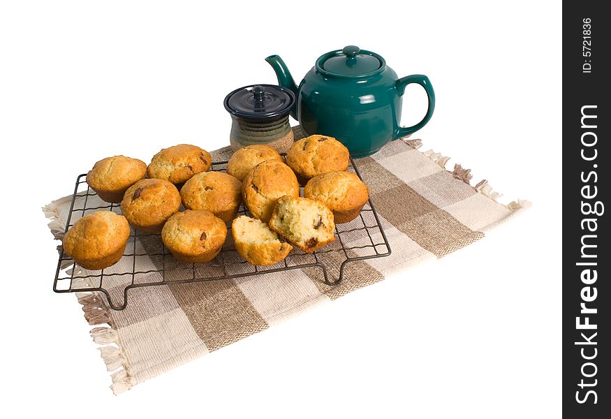 Freshly baked chocolate chip muffins on cooling rack with teapot isolated on white background.