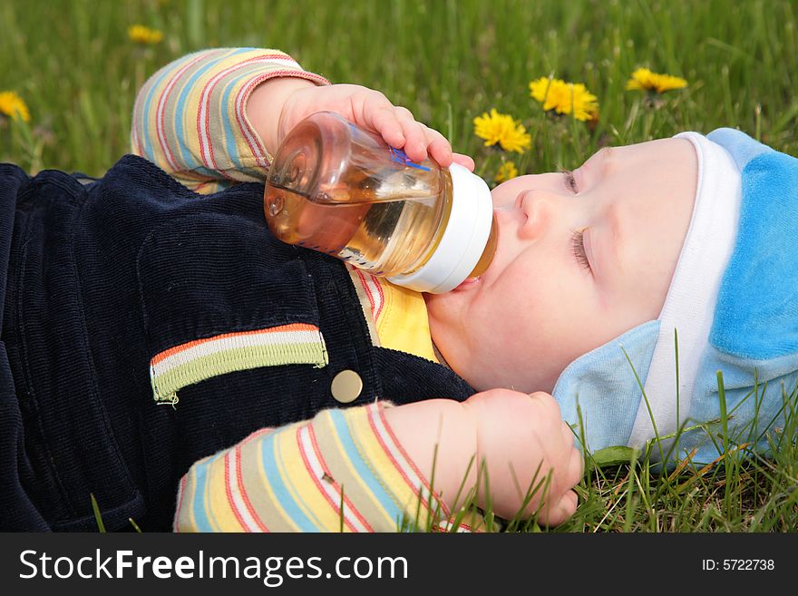 Child Drinks From A Bottle Laying In  Grass