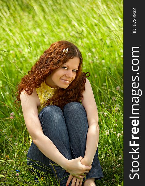 The beautiful young girl sits on a background of a green lawn and smiles. The beautiful young girl sits on a background of a green lawn and smiles