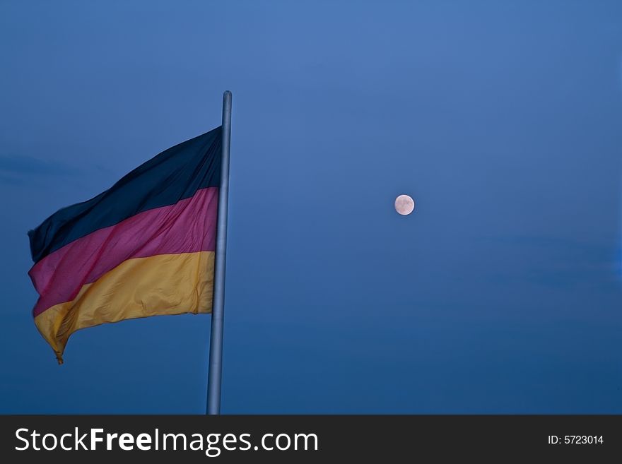 The German flag and the moon against a blue dusk sky. The German flag and the moon against a blue dusk sky.
