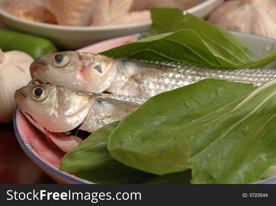 Two fishes and green vegetable in the dish, ready for cooking. Two fishes and green vegetable in the dish, ready for cooking.