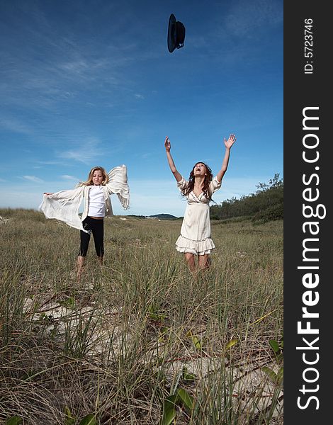 Two girls having fun running and throwing up hats in a dry countryside field. Two girls having fun running and throwing up hats in a dry countryside field