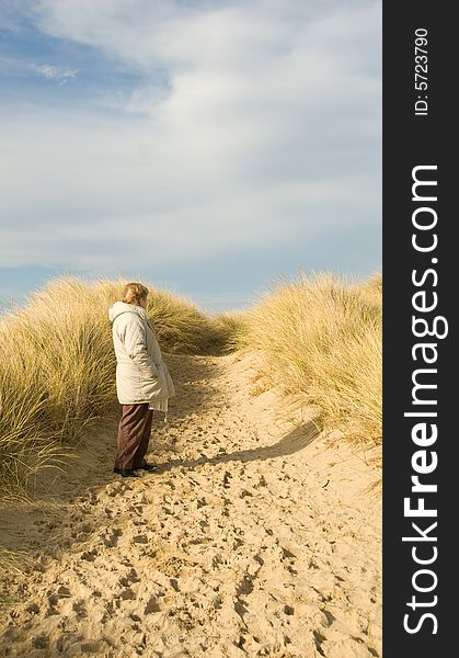 A senior lady standing on a sandy track in the sand dunes. A senior lady standing on a sandy track in the sand dunes.