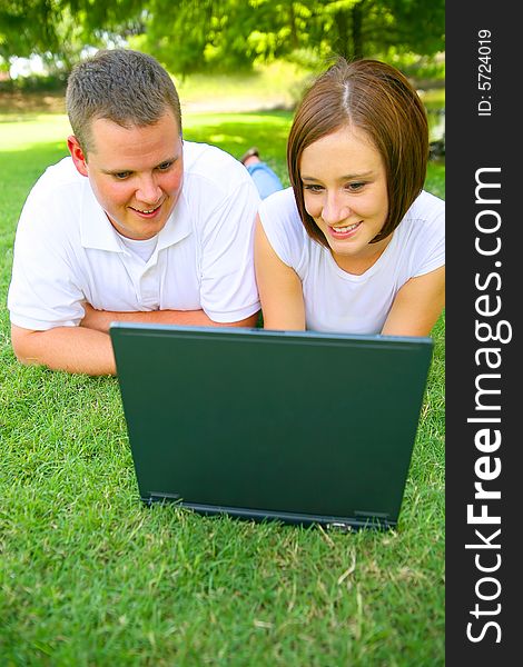 Caucasian couple using or working with computer outdoor on the grass. Caucasian couple using or working with computer outdoor on the grass