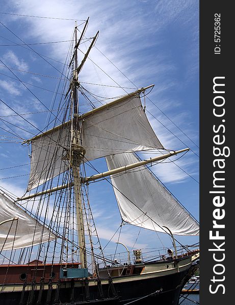 A white ship mast with sails against a bright blue sky