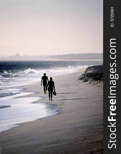 Two lonely figures walking down the beach shoreline on a windy day.