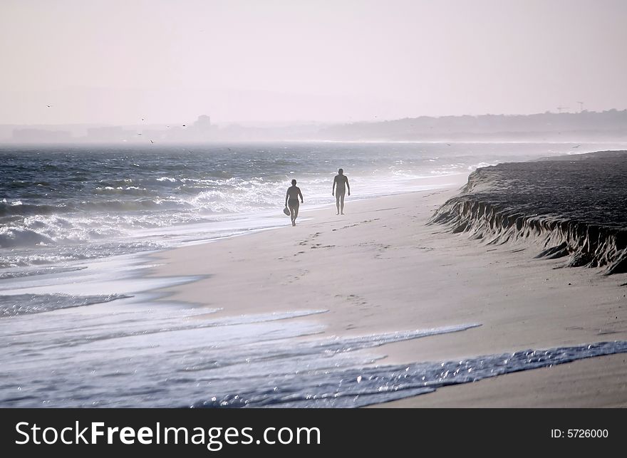 Two lonely figures walking side-by-side on the beach shoreline on a windy day. Two lonely figures walking side-by-side on the beach shoreline on a windy day.