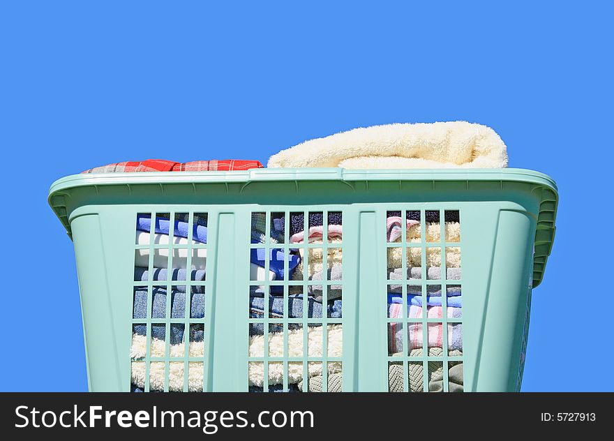 Neatly folded laundry in green plastic laundry hamper against blue background. Neatly folded laundry in green plastic laundry hamper against blue background