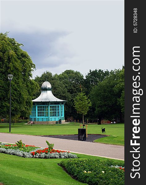 A park's green space with trees and grass, with a bandstand and a dog running with a ball. A park's green space with trees and grass, with a bandstand and a dog running with a ball.