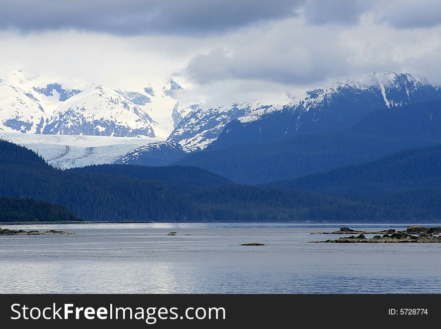 Moody seascape across alaskan bay with clouds and snow capped mountains in background. Moody seascape across alaskan bay with clouds and snow capped mountains in background