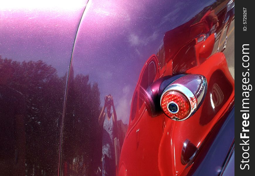 A purple car with tail light. Self portrait of photographer and red car reflection.