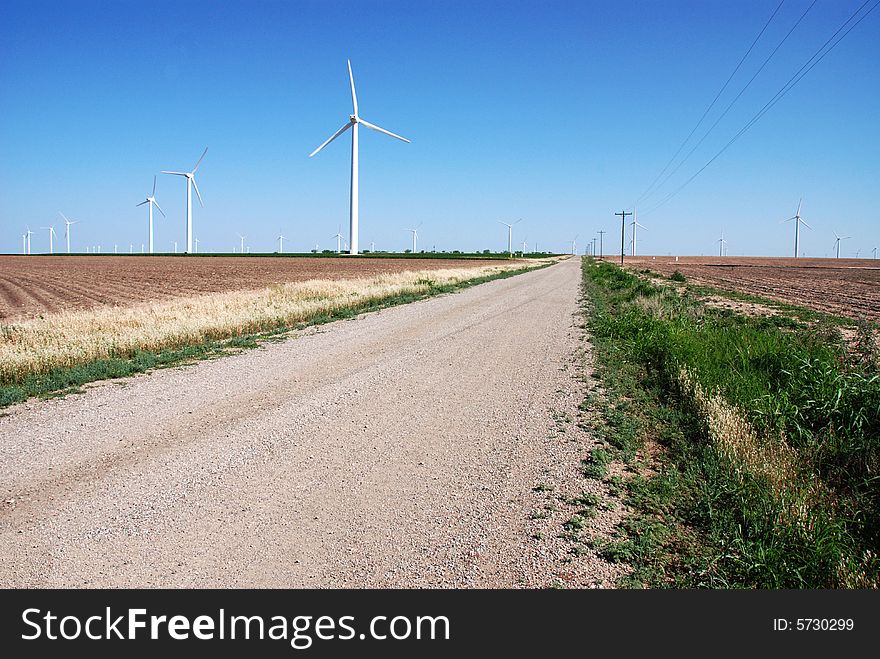 Numerous wind turbines in plowed fields with a graveled country road going through them. Numerous wind turbines in plowed fields with a graveled country road going through them