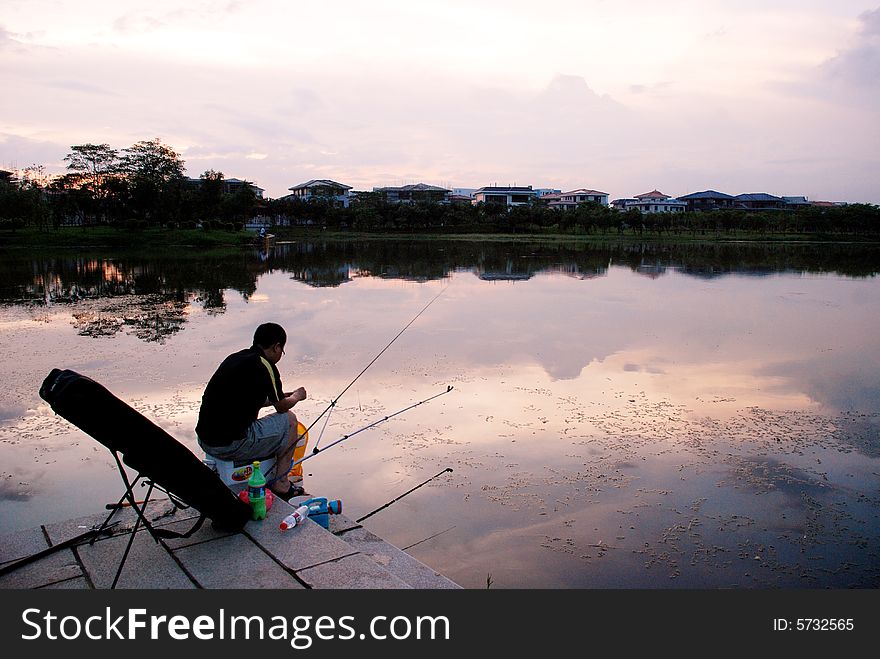 An asian man angling in the sunset by the lakeside.