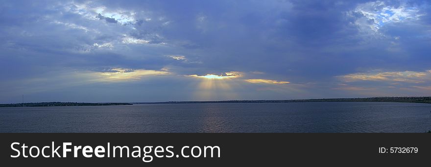 Panorama of evening river and cloudy sky with sunbeams