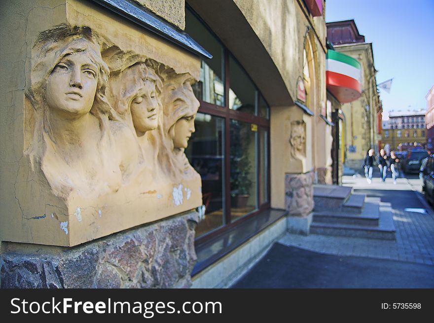 Entrance to cafe in city street with a group of people in background. The building was built before 1900, and the sculptures on the facade are public monuments and nobody can have copyright on them.