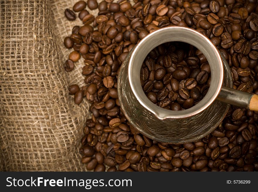 Cezve with freshly roasted coffee beans on sackcloth. Shallow depth of field. Focus on cezve throat