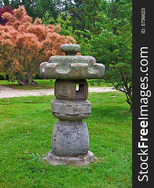 Japanese lantern in stroll garden with decorative background trees.