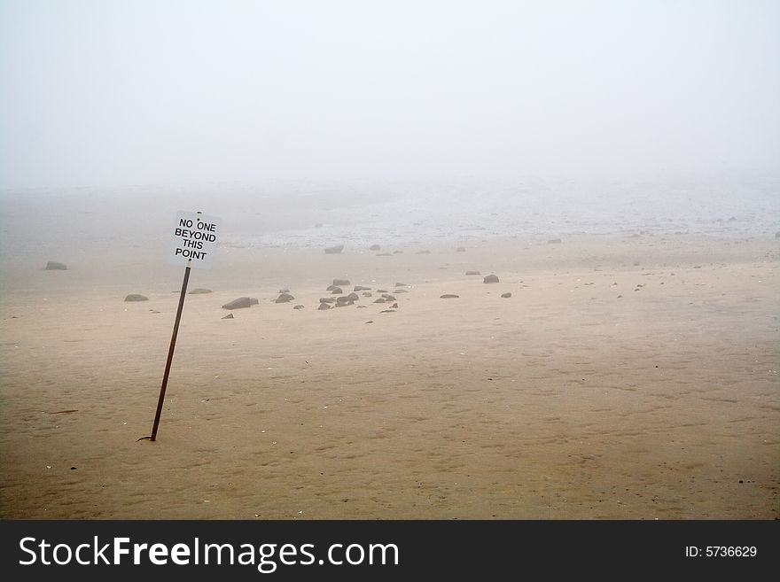 Foggy view of beach with warning sign for swimmers.