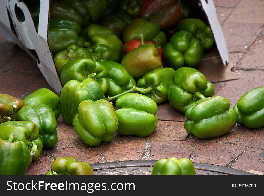 Fresh green peppers spilling out of box onto brick sidewalk