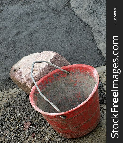 A shot of a bucket for the cement and some stones for a wall in a work place. A shot of a bucket for the cement and some stones for a wall in a work place