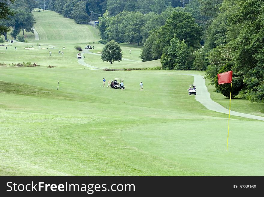 A view down a long fairway with carts and golfers. A view down a long fairway with carts and golfers