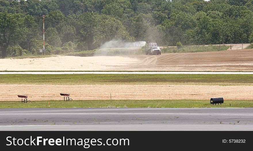 A water truck wetting down a construction site by an airplane runway. A water truck wetting down a construction site by an airplane runway