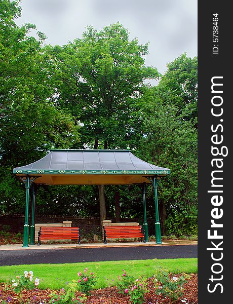 A photograph of a shelter in a park with two wooden benches. A photograph of a shelter in a park with two wooden benches