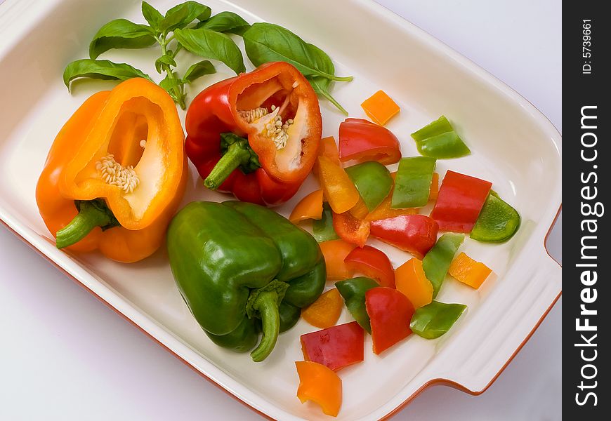 Three peppers cut in preparation in a white dish with basil leaves. Three peppers cut in preparation in a white dish with basil leaves.