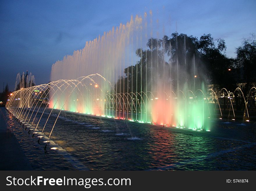 A fountain at night being illuminated with lots of colors.