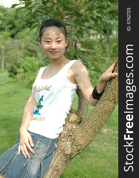 Chinese girl smiling and sitting on tree in park. Chinese girl smiling and sitting on tree in park.