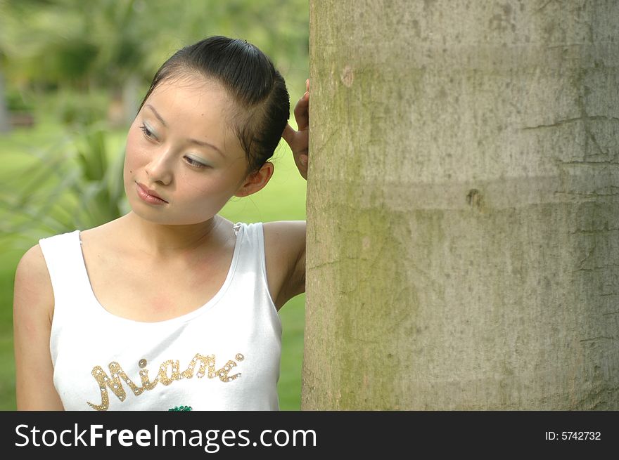 Chinese girl standing near palm tree in park, thoughtful. Chinese girl standing near palm tree in park, thoughtful.