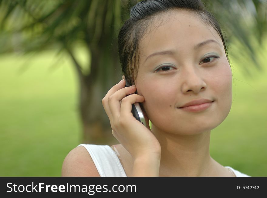 Chinese girl in park, holding mobile phone with kind looks. Chinese girl in park, holding mobile phone with kind looks.