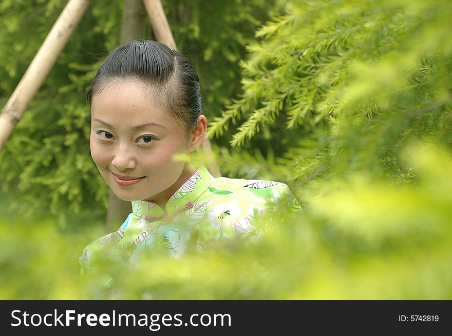 Chinese girl standing between green leafs in park, wearing traditional dress. Chinese girl standing between green leafs in park, wearing traditional dress.