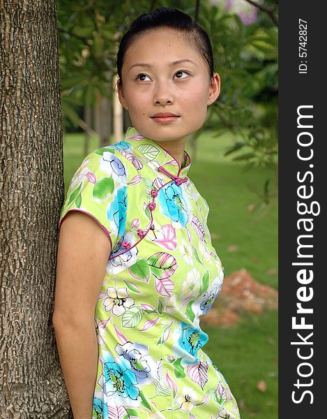 Chinese girl in traditional dress - QiPan, leaning on tree in park, thoughtful face expression. Chinese girl in traditional dress - QiPan, leaning on tree in park, thoughtful face expression.