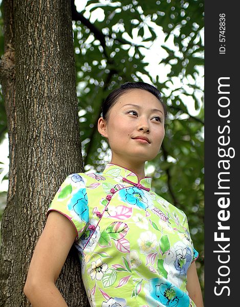 Chinese girl in traditional dress - QiPan, leaning on tree in park, thoughtful face expression. Chinese girl in traditional dress - QiPan, leaning on tree in park, thoughtful face expression.