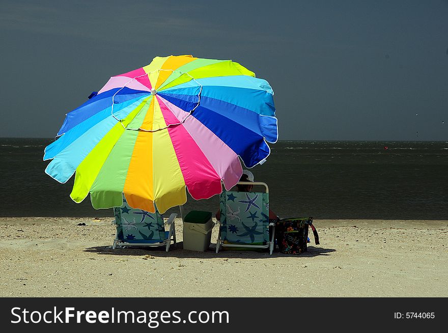 Woman sitting under colorful parasol on white sandy beach. Woman sitting under colorful parasol on white sandy beach