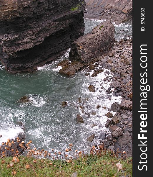 Looking down from the cliff top the waves are swirling around the rocks.  A large dark rock looms upward.  Do you have vertigo or a good head for heights? On the coast, sea cliffs can be dangerous.